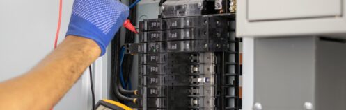 Electrician is using a digital meter to measure the voltage at the circuit breaker control cabinet on the wall.