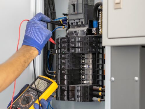 Electrician is using a digital meter to measure the voltage at the circuit breaker control cabinet on the wall.